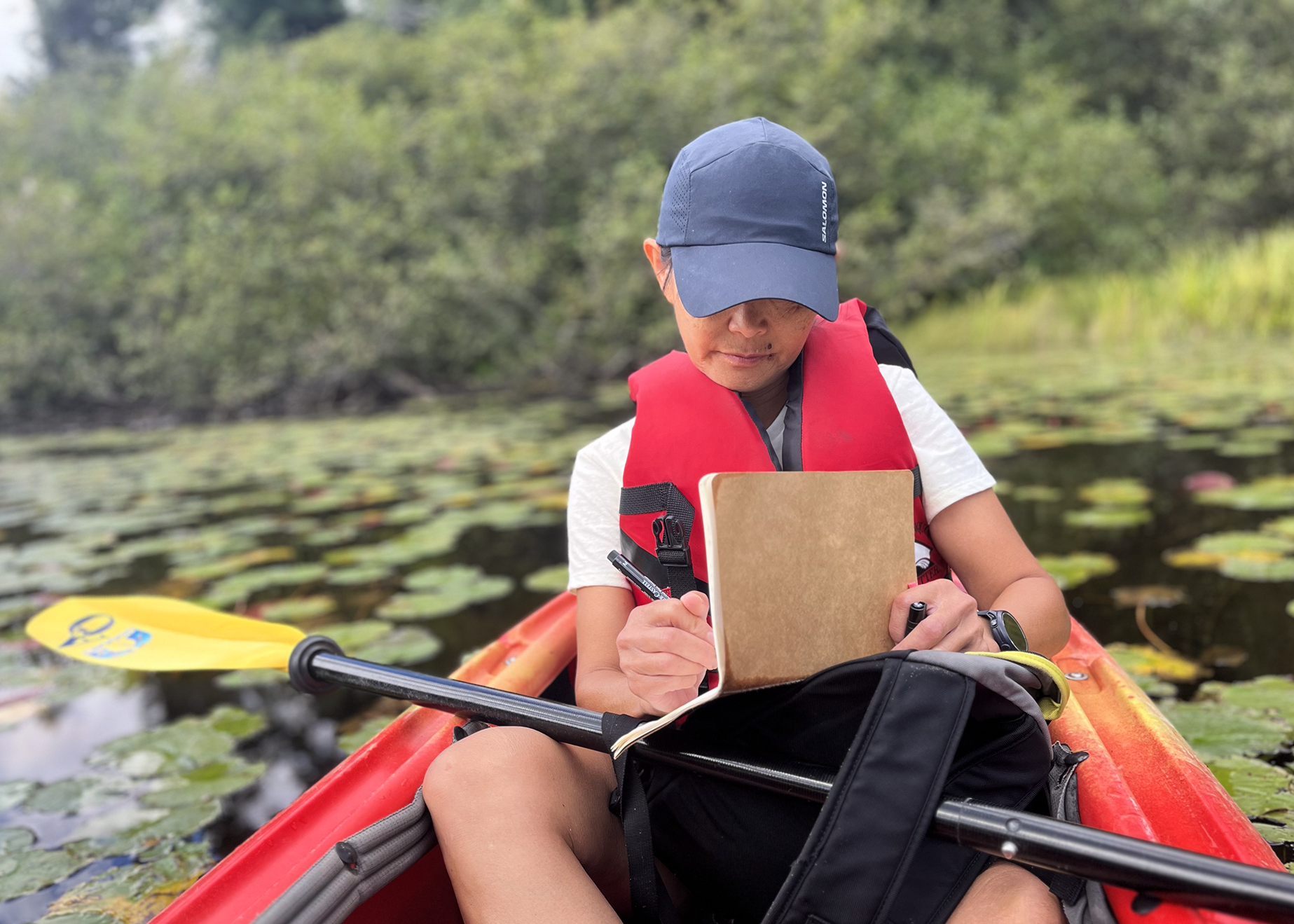 Christina Blackley sitting in a kayak on a river drawing